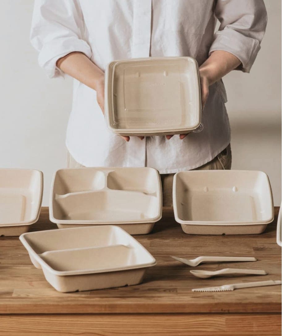 A Safra team member holding a compostable fiber container above a table of bagasse trays